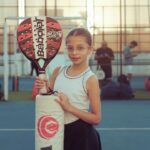 Een jonge speler met een lichtgewicht kinderpadelracket in actie op de tennisbaan.